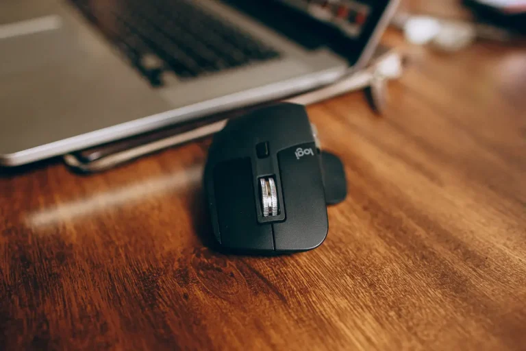 Ergonomiczna mysz komputerowa i laptop na drewnianym biurku.